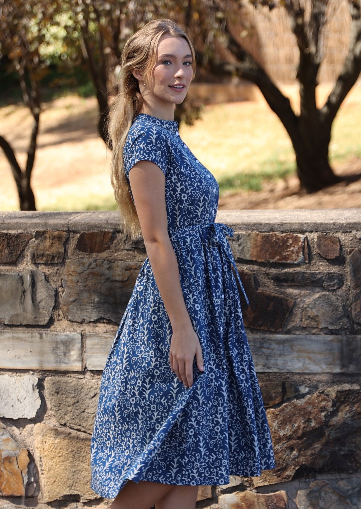 Woman stands side on in cotton 50's style midi length dress with cap sleeves and waist tie