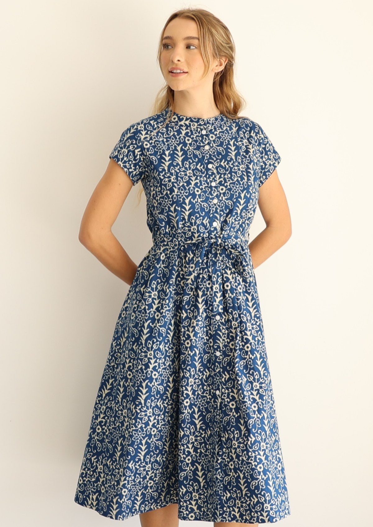 Woman wears 50's style cotton button through midi length dress with high round neckline and waist tie