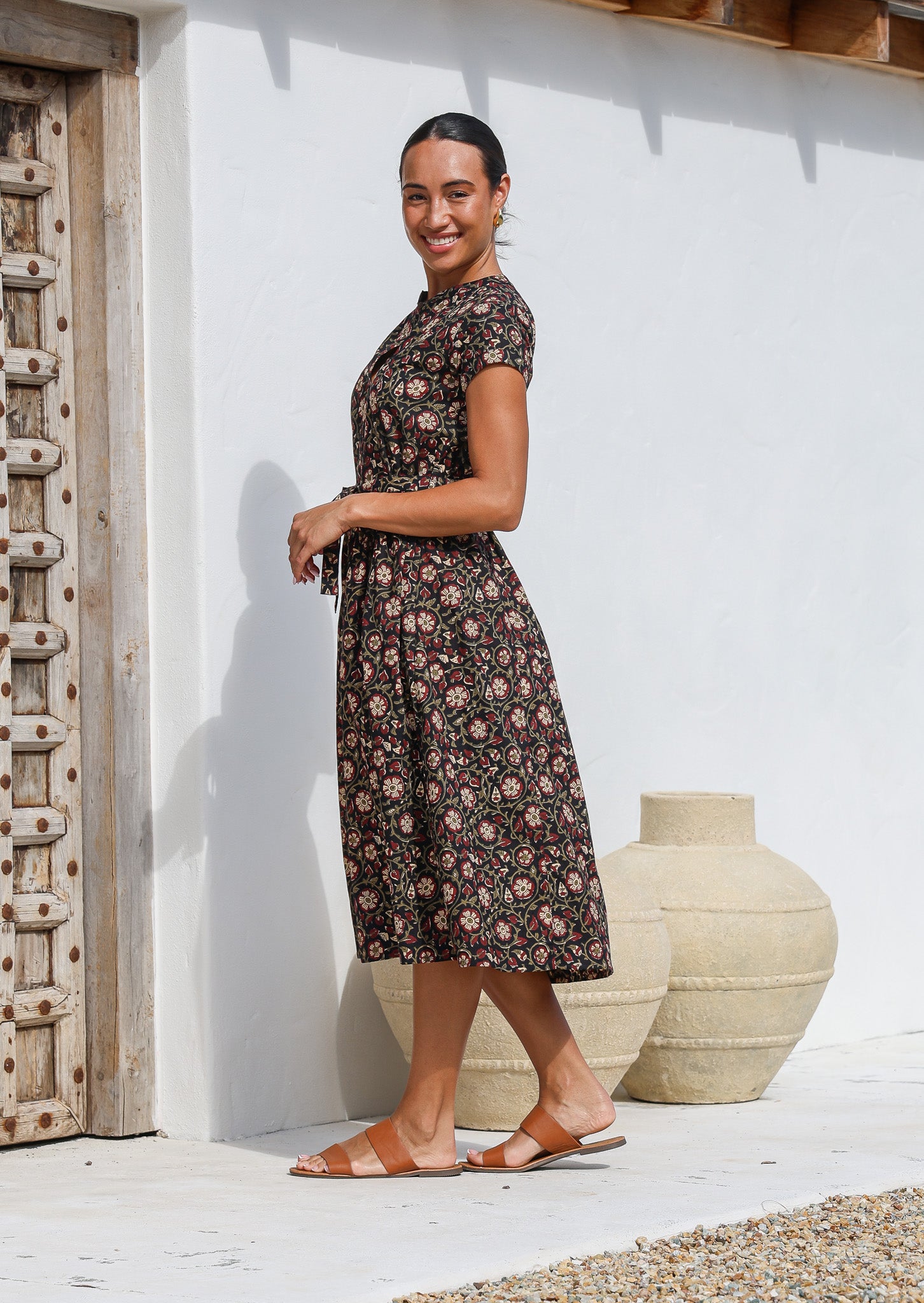 Women stands in side pose wearing floral printed midi length dress with high round neckline, short sleeves and pockets.