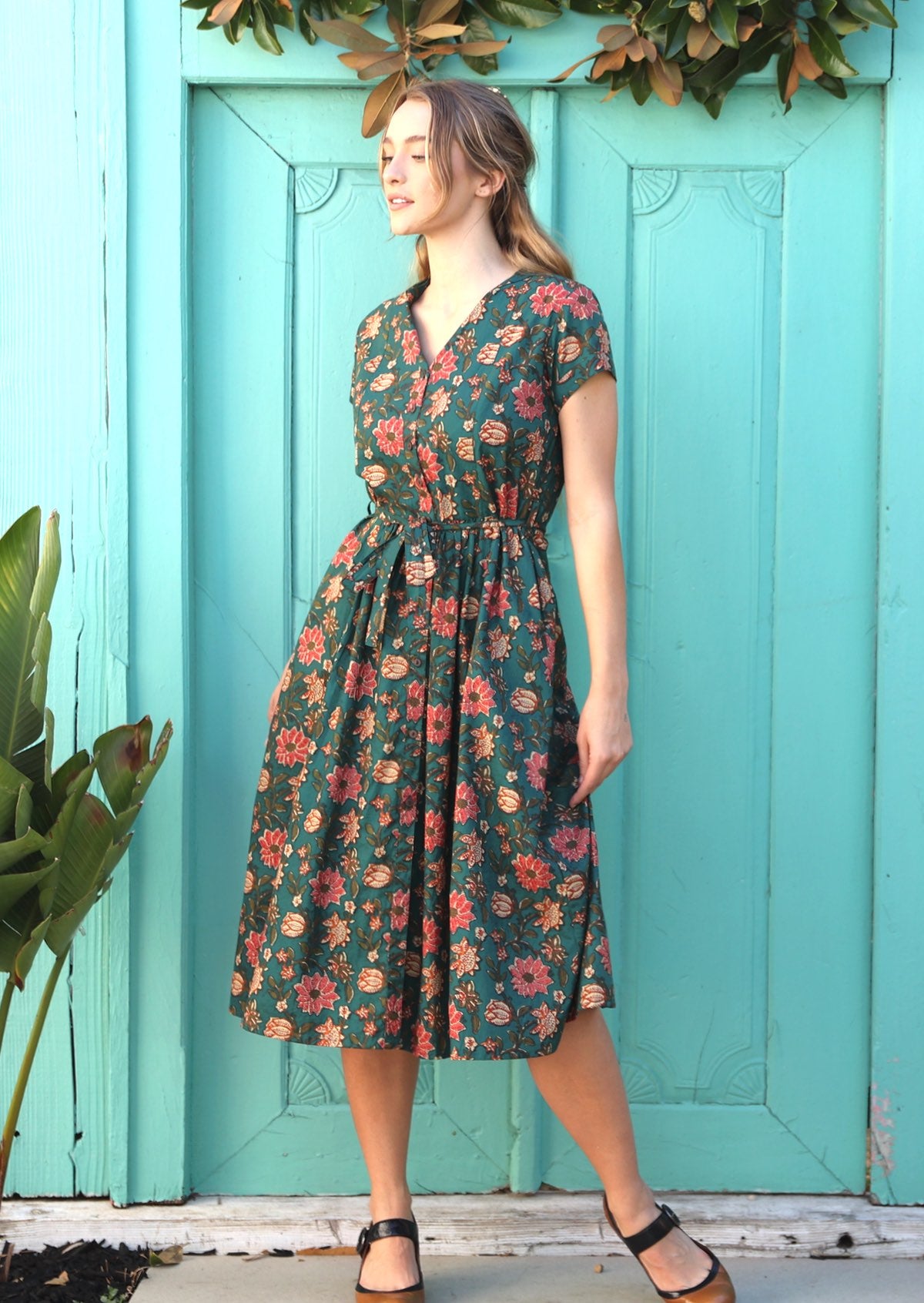 Woman standing in green cotton floral maxi dress with mandarin collar and waist tie.