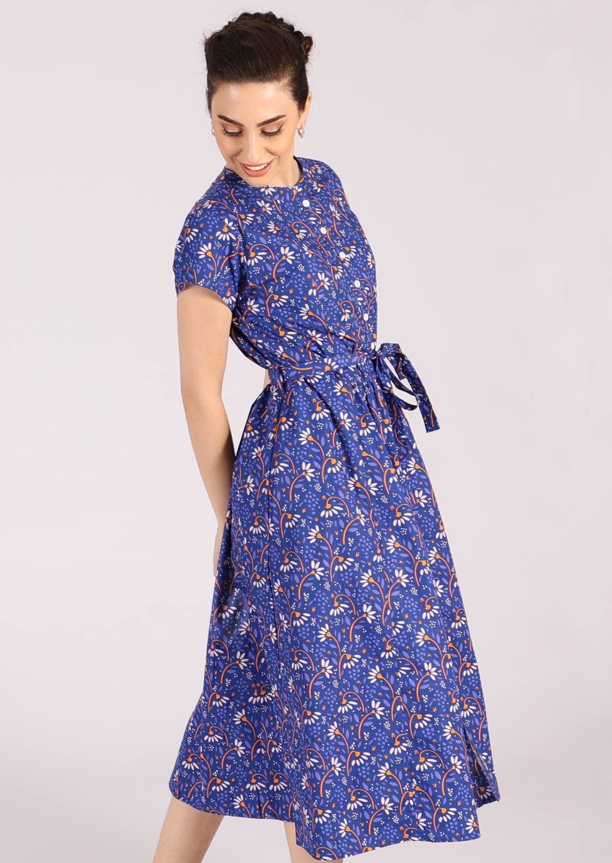 Model wears a long retro style dress with pleats at the waist. 