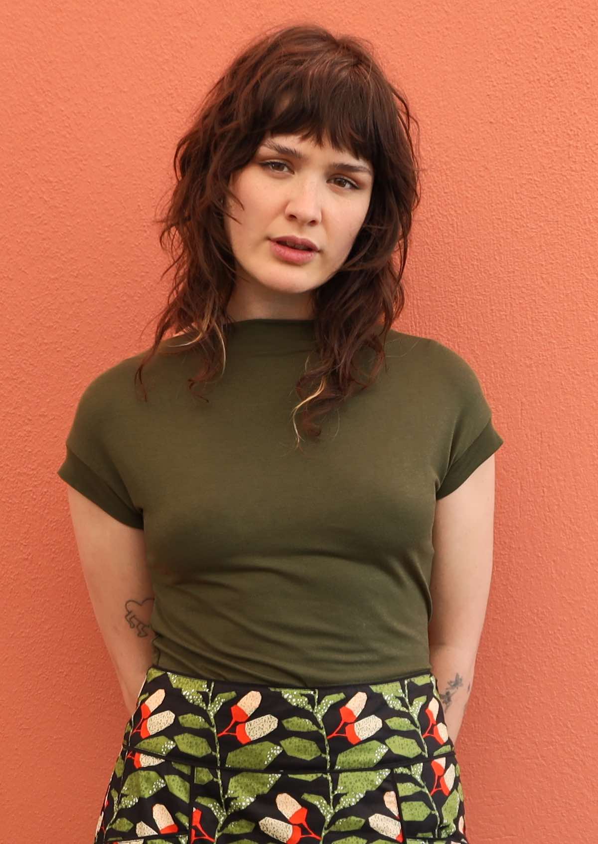 Woman wearing a wide neck mod olive green stretch rayon boat neck top with floral skirt.