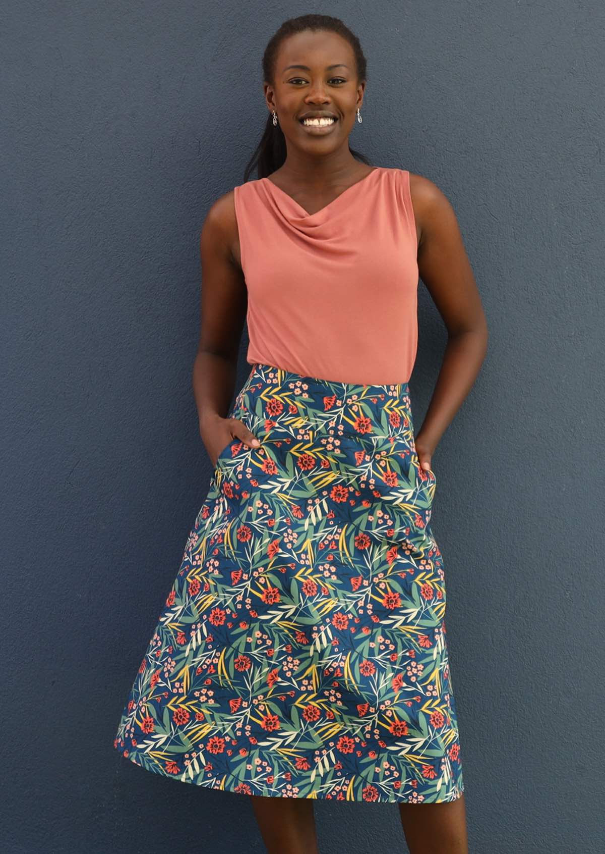 Model has hands in the pockets of her floral skirt. 