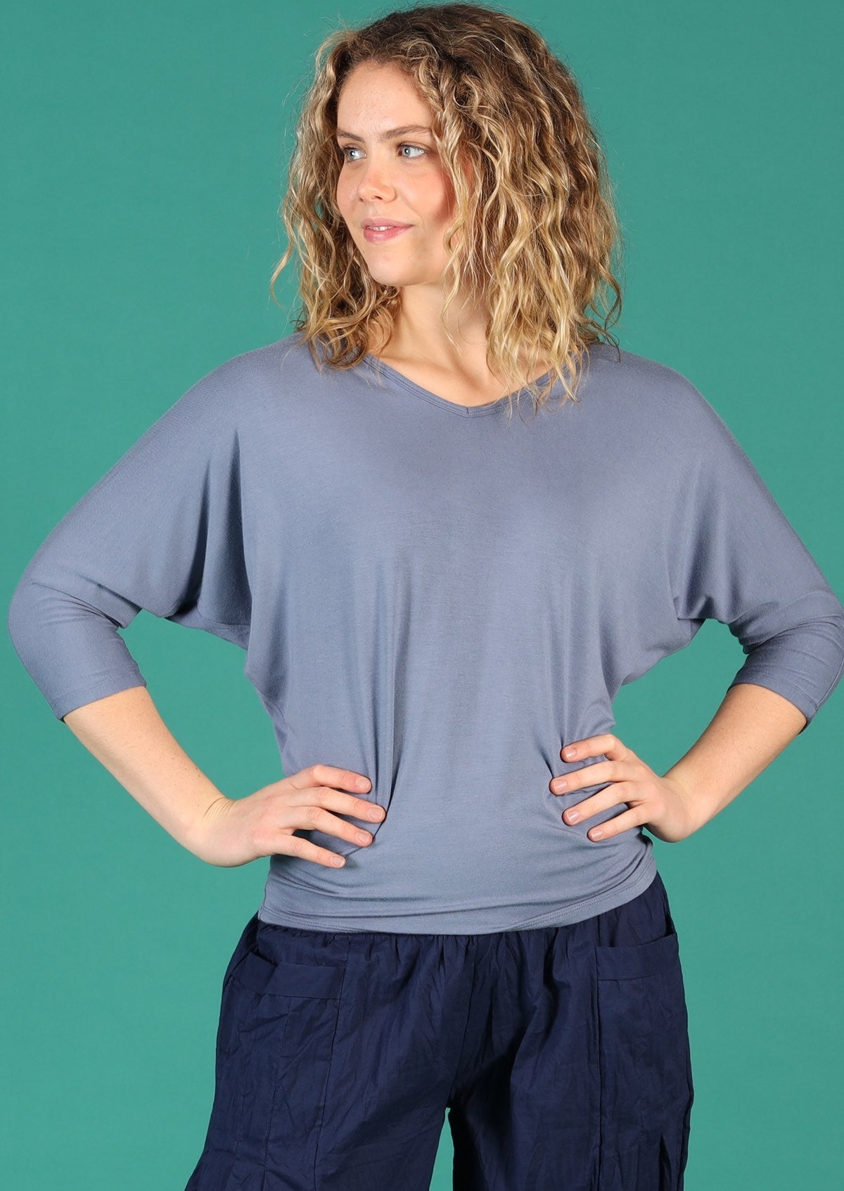 Woman wearing a 3/4 sleeve rayon batwing v-neck grey top with navy pants.