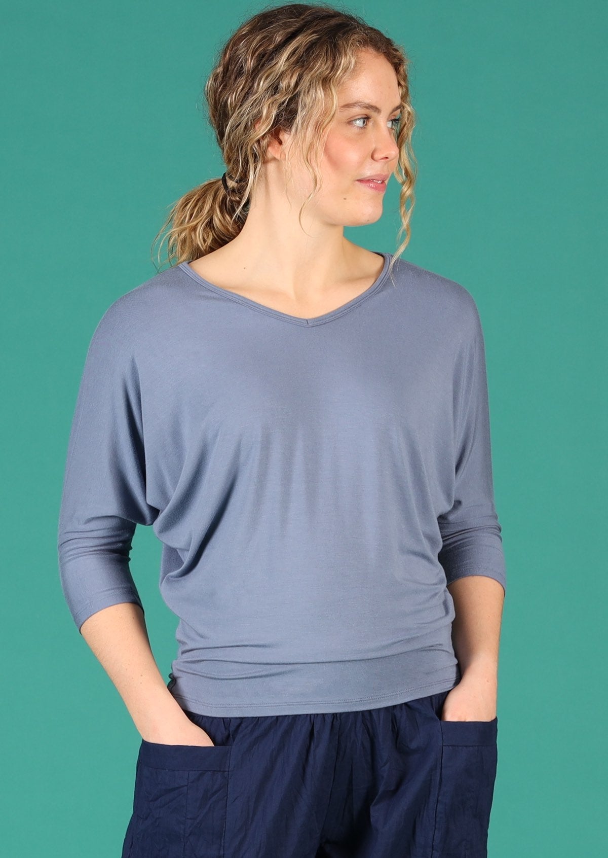 Woman with blonde curly hair wearing a 3/4 sleeve rayon batwing v-neck grey top.