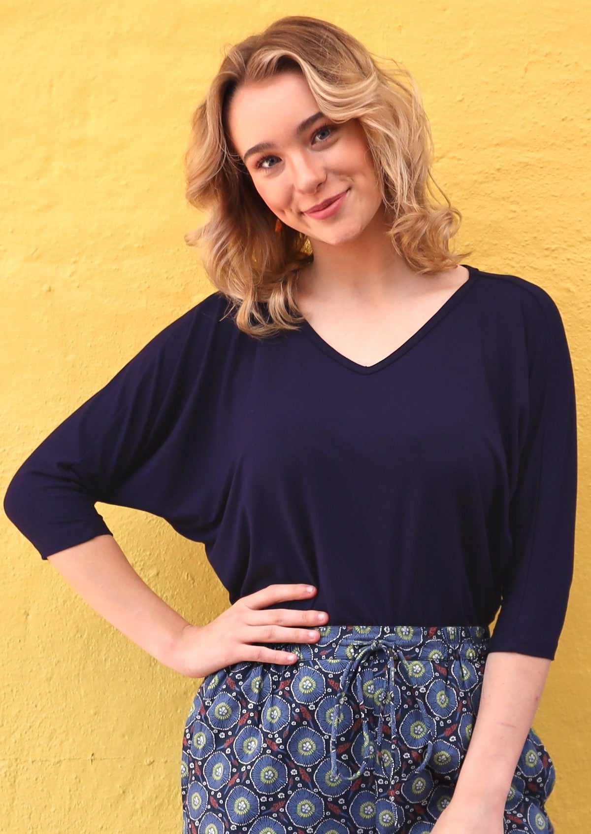 Woman wearing a 3/4 sleeve rayon batwing v-neck navy blue top with high waisted blue pants.