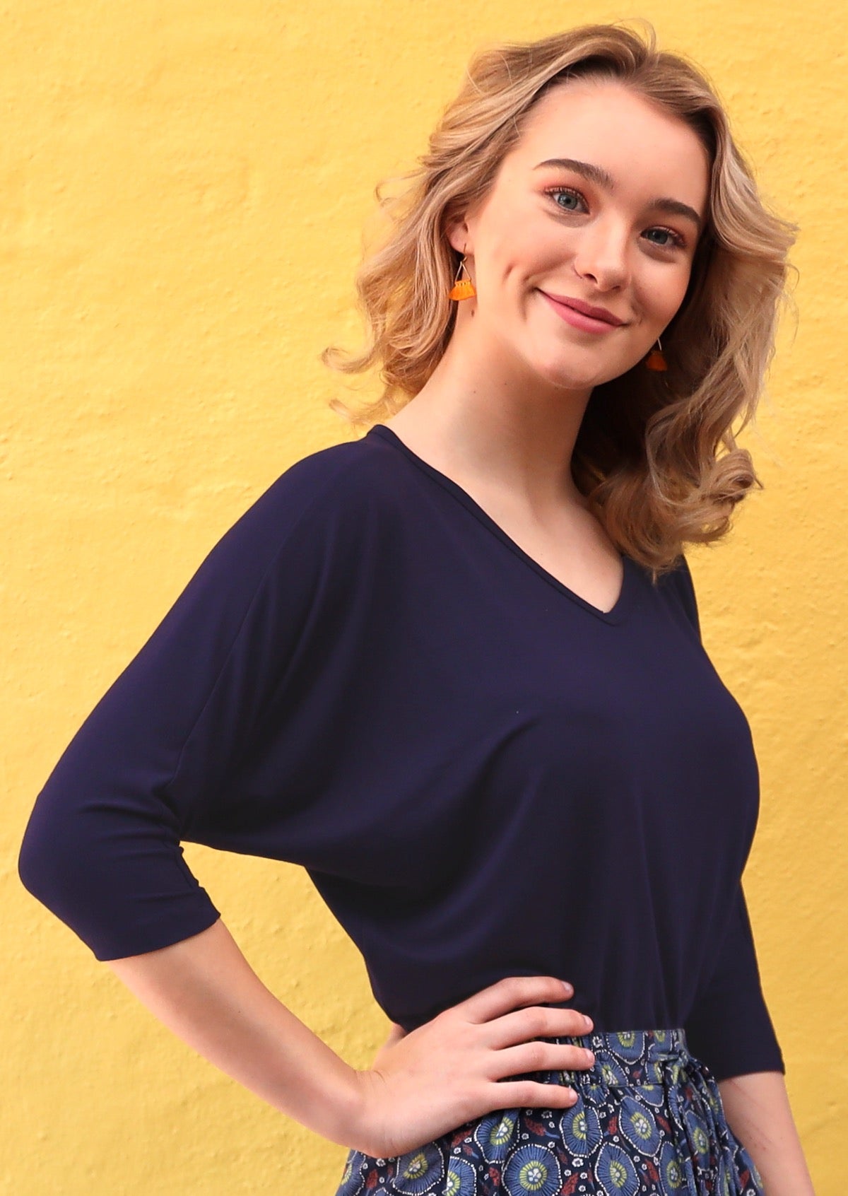 Woman with light brown hair wearing a 3/4 sleeve rayon batwing v-neck navy blue top.