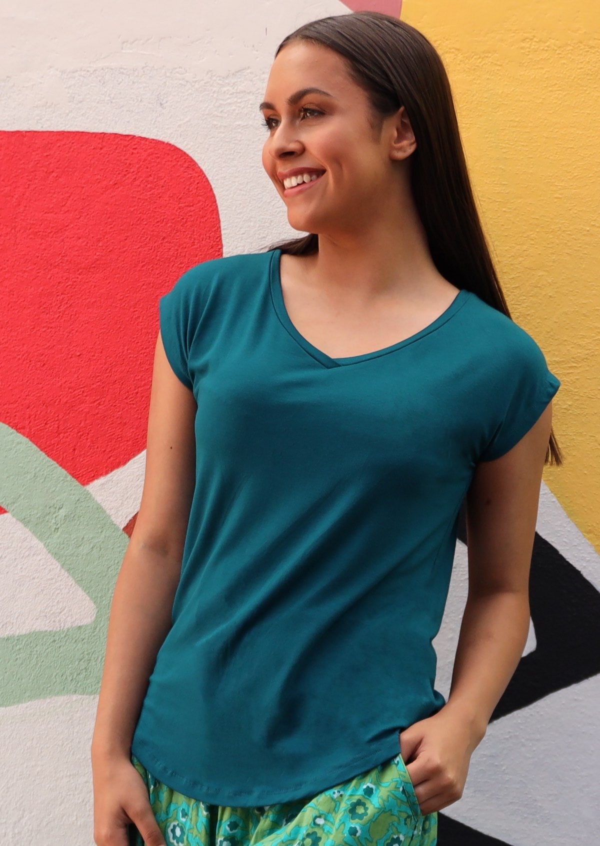 Woman with dark hair wearing a teal v-neck short cap sleeve rayon top.