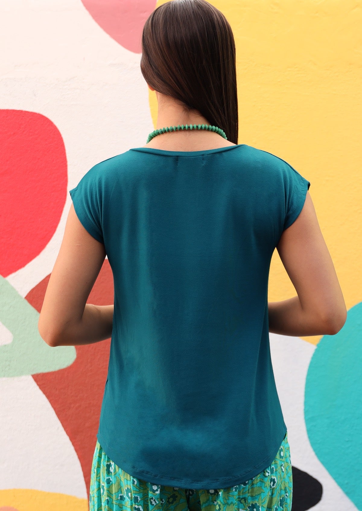 Back view of a woman wearing a teal v-neck short cap sleeve rayon top.