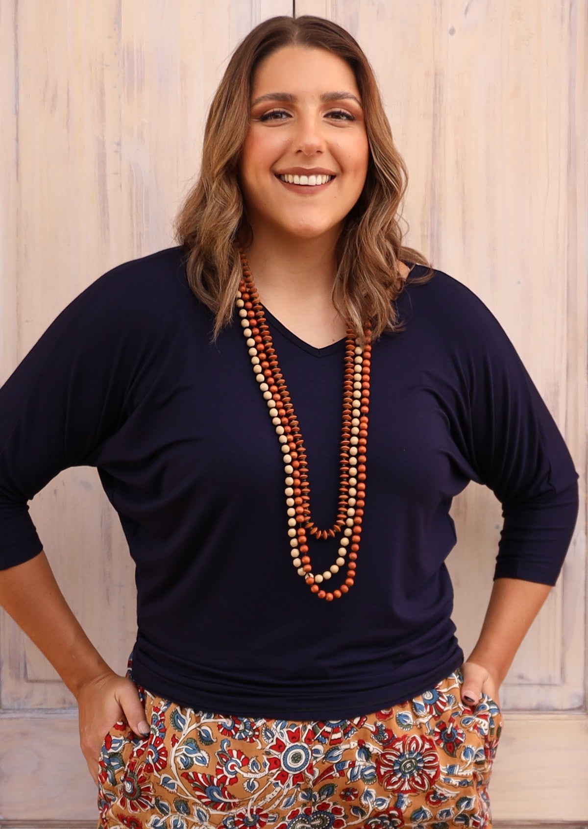 Woman wearing a 3/4 sleeve rayon batwing v-neck navy blue top with wooden beads.
