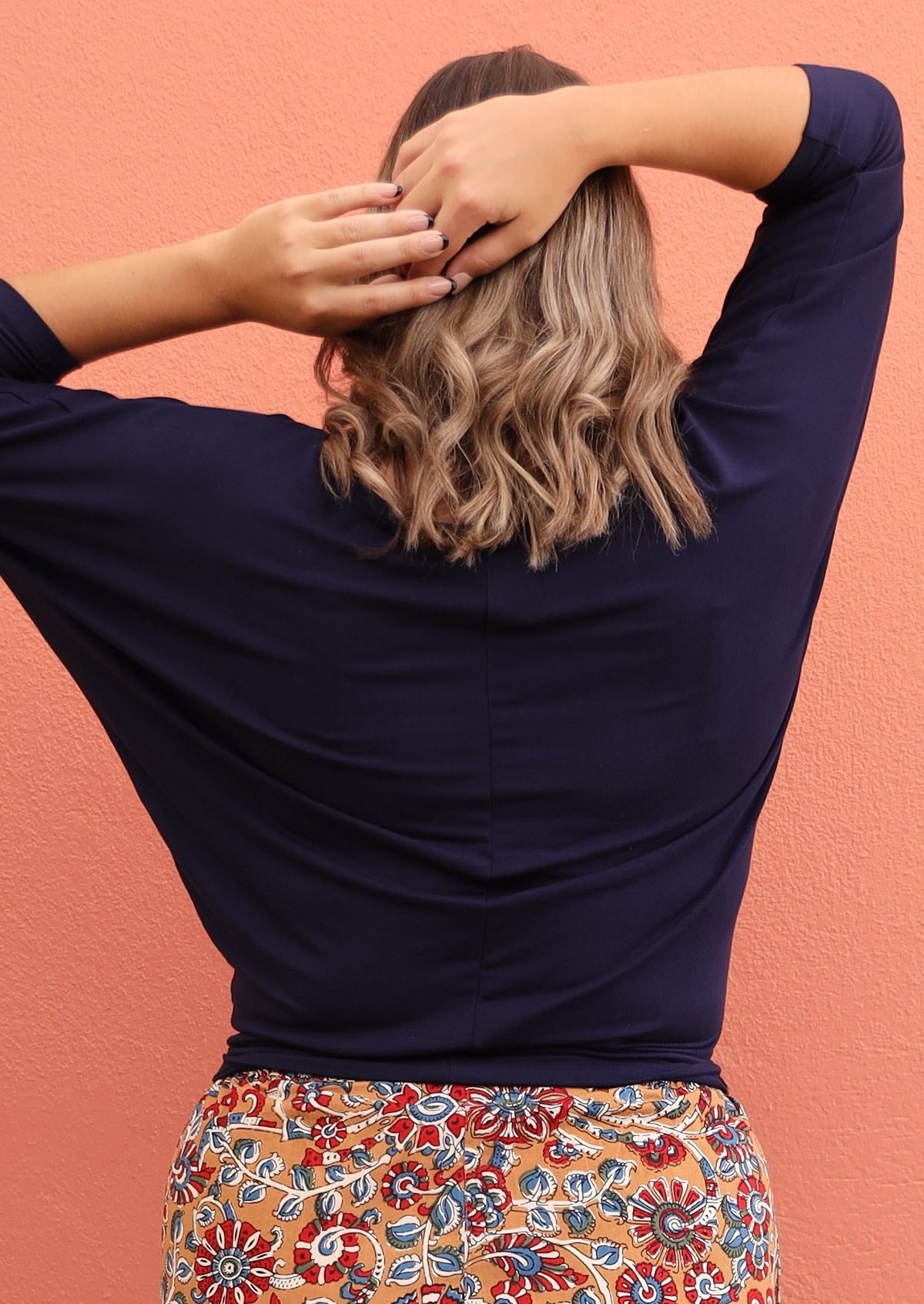 Back view of a woman wearing a 3/4 sleeve rayon batwing v-neck navy blue top.