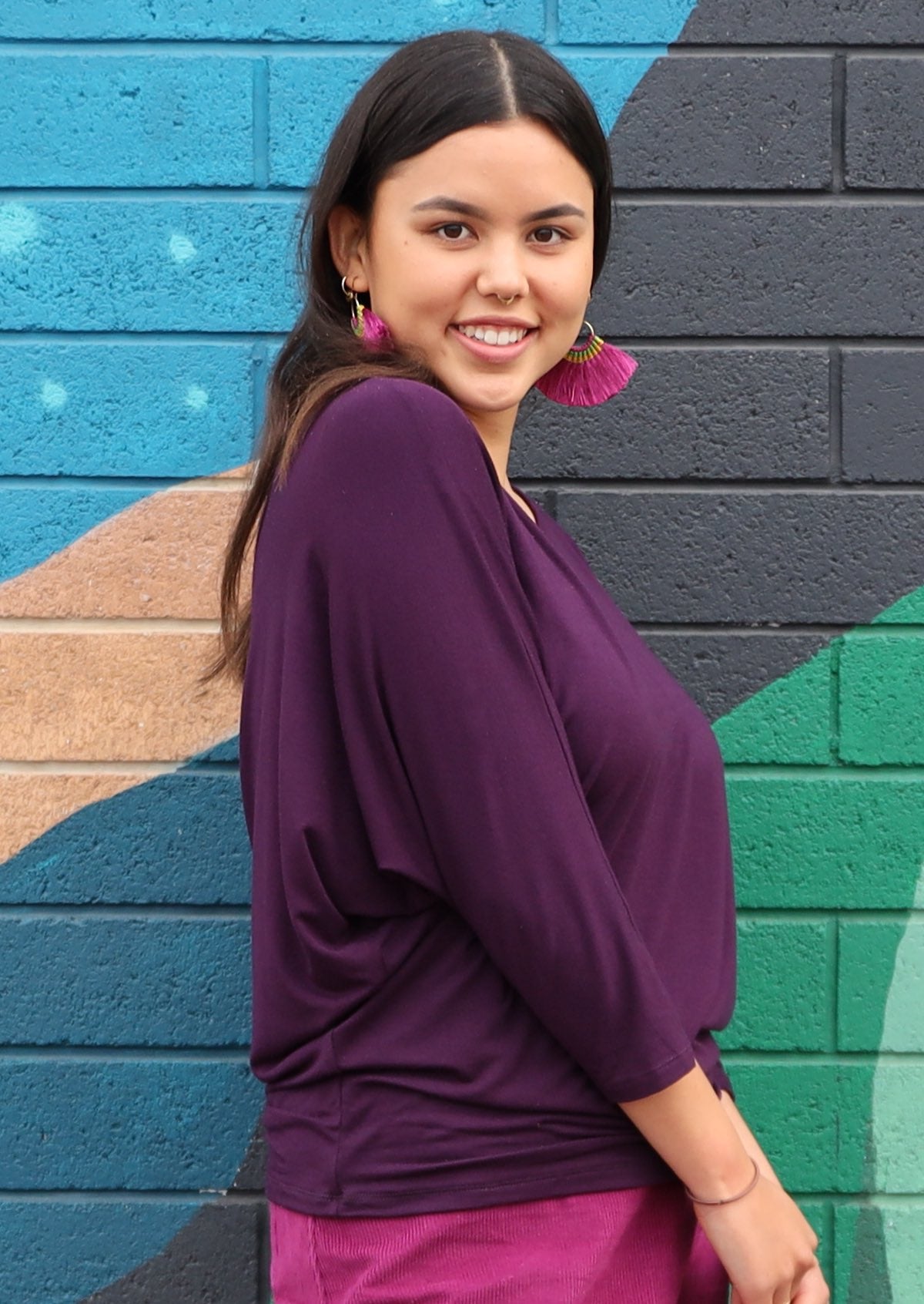 Side view of woman wearing a 3/4 sleeve rayon batwing round neckline purple top.