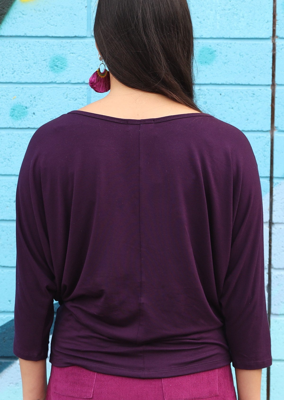 Back view of woman wearing a 3/4 sleeve rayon batwing round neckline purple top.