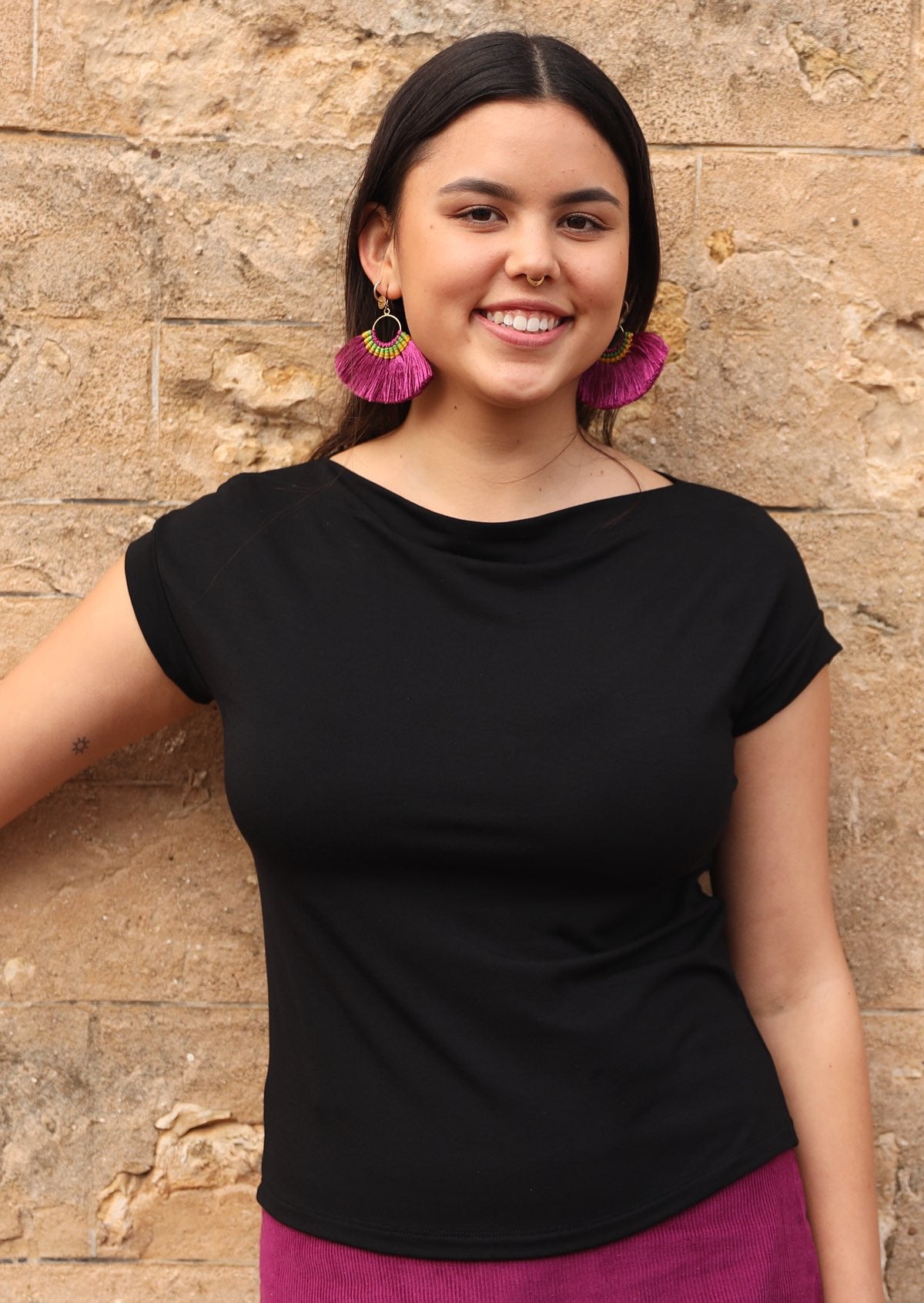Front view of a woman wearing a wide neck mod black stretch rayon boat neck top with a purple skirt and earrings.
