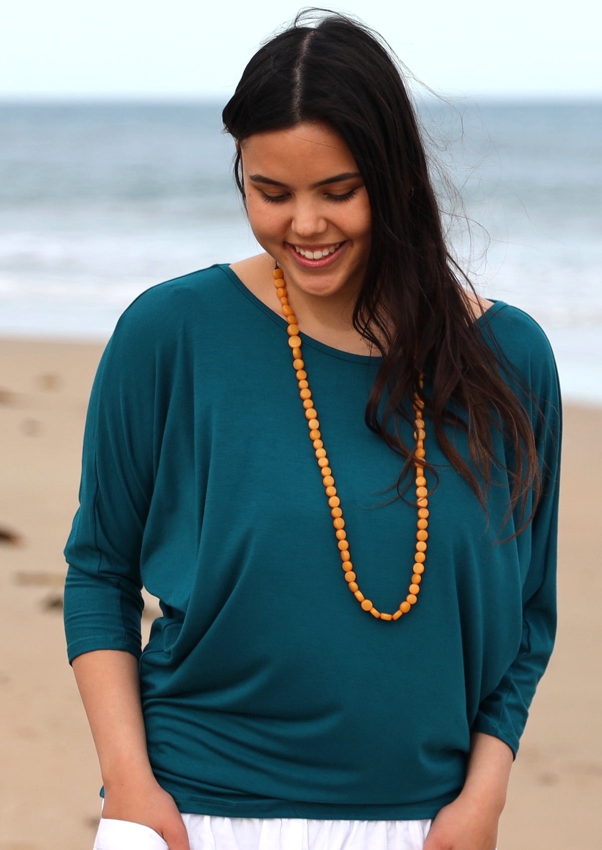 Woman with dark hair looking down wearing a 3/4 sleeve rayon batwing round neckline teal top.