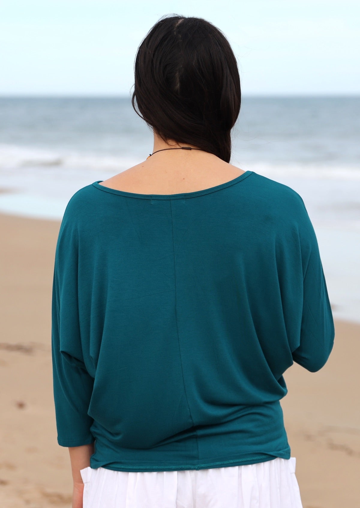 Back view of a woman wearing a 3/4 sleeve rayon batwing round neckline teal top.