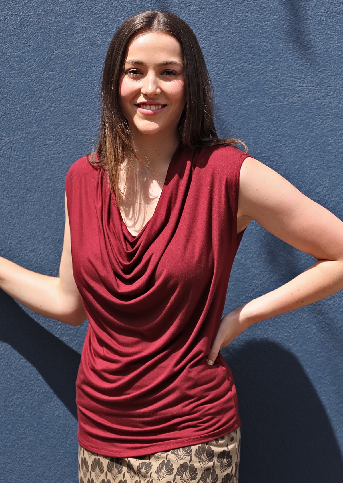 Woman with dark hair wearing a cowl neck rayon maroon cap sleeve top.
