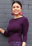Woman wearing a rayon boat neck purple 3/4 sleeve top and purple earrings.