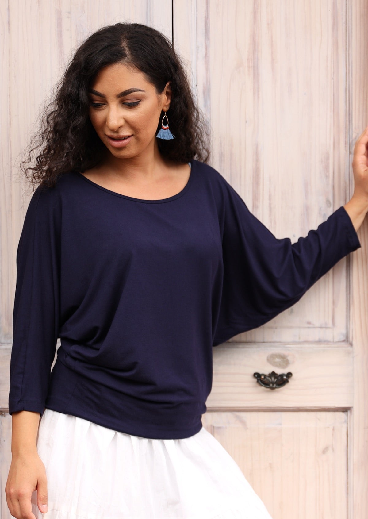 Woman wearing a 3/4 sleeve rayon batwing round neckline navy blue top and blue earrings.
