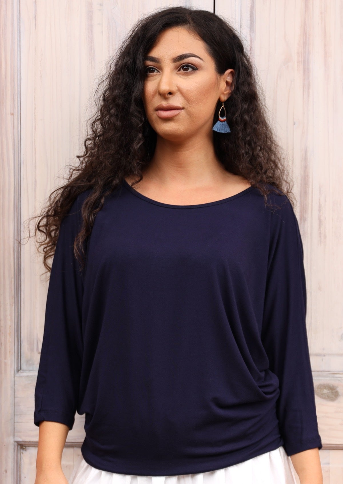 Woman with dark curly hair wearing a 3/4 sleeve rayon batwing round neckline navy blue top.