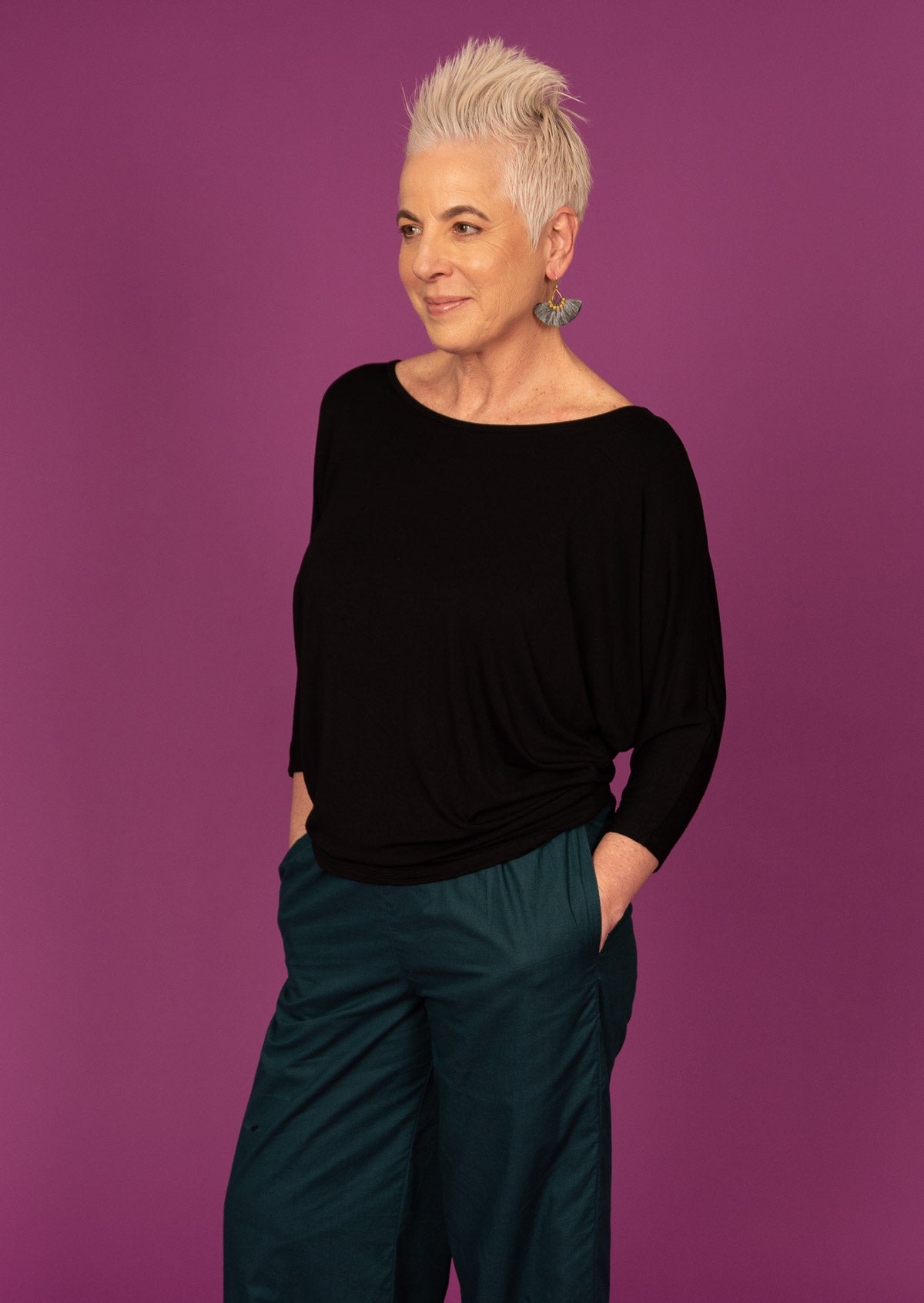 Woman wearing a 3/4 sleeve rayon batwing round neckline black top on purple background.