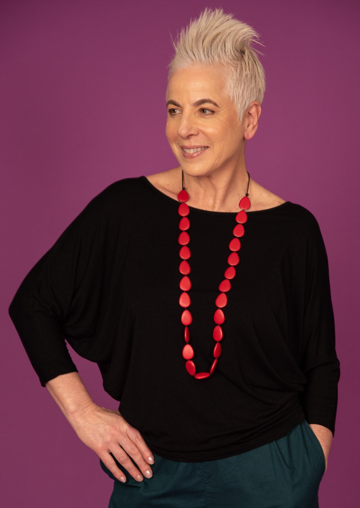 Woman wearing a 3/4 sleeve rayon batwing round neckline black top with red beads.