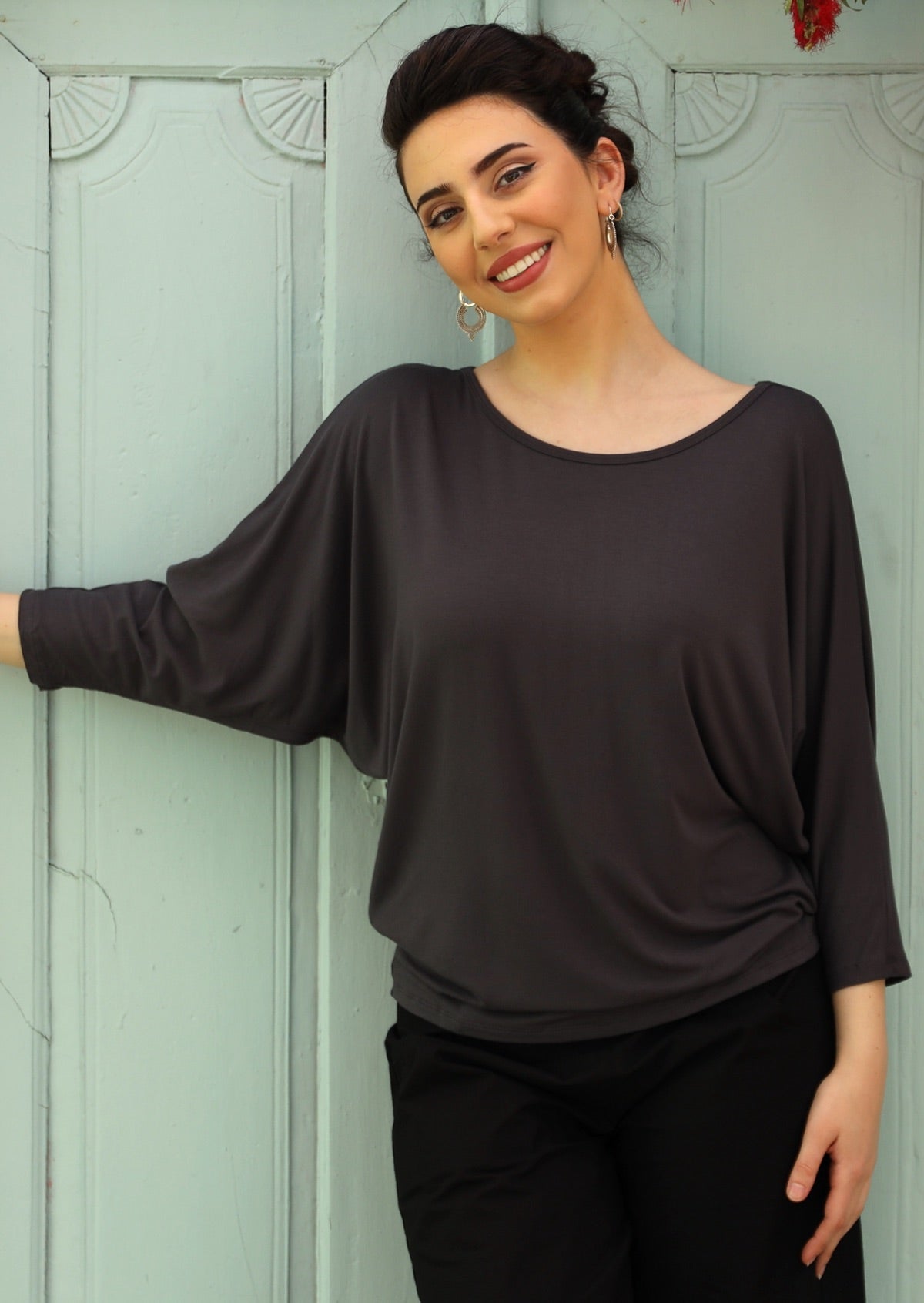 Woman wearing a 3/4 sleeve rayon batwing round neckline dark grey top with black pants.