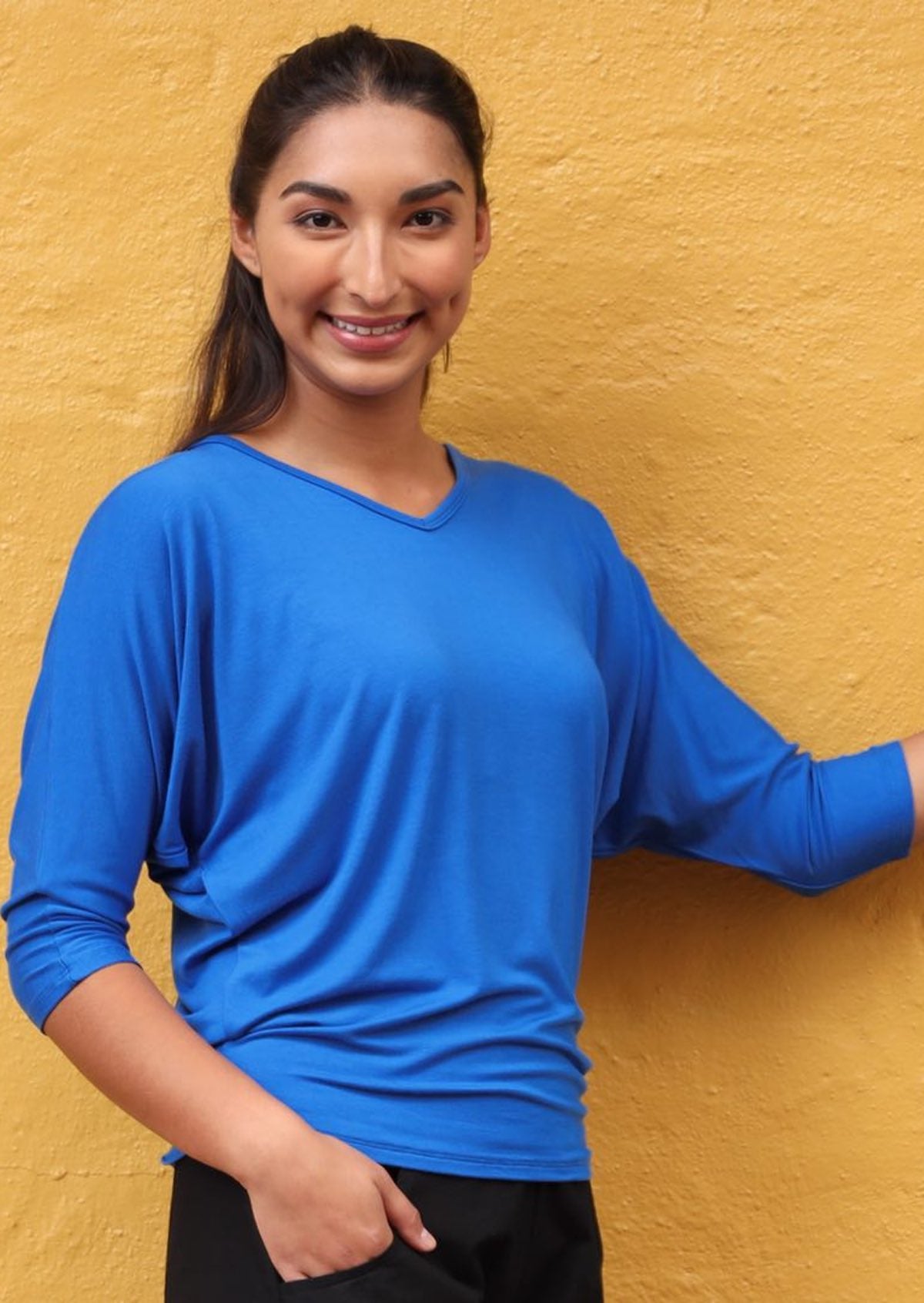 Woman wearing a 3/4 sleeve rayon batwing v-neck blue top in front of orange wall.