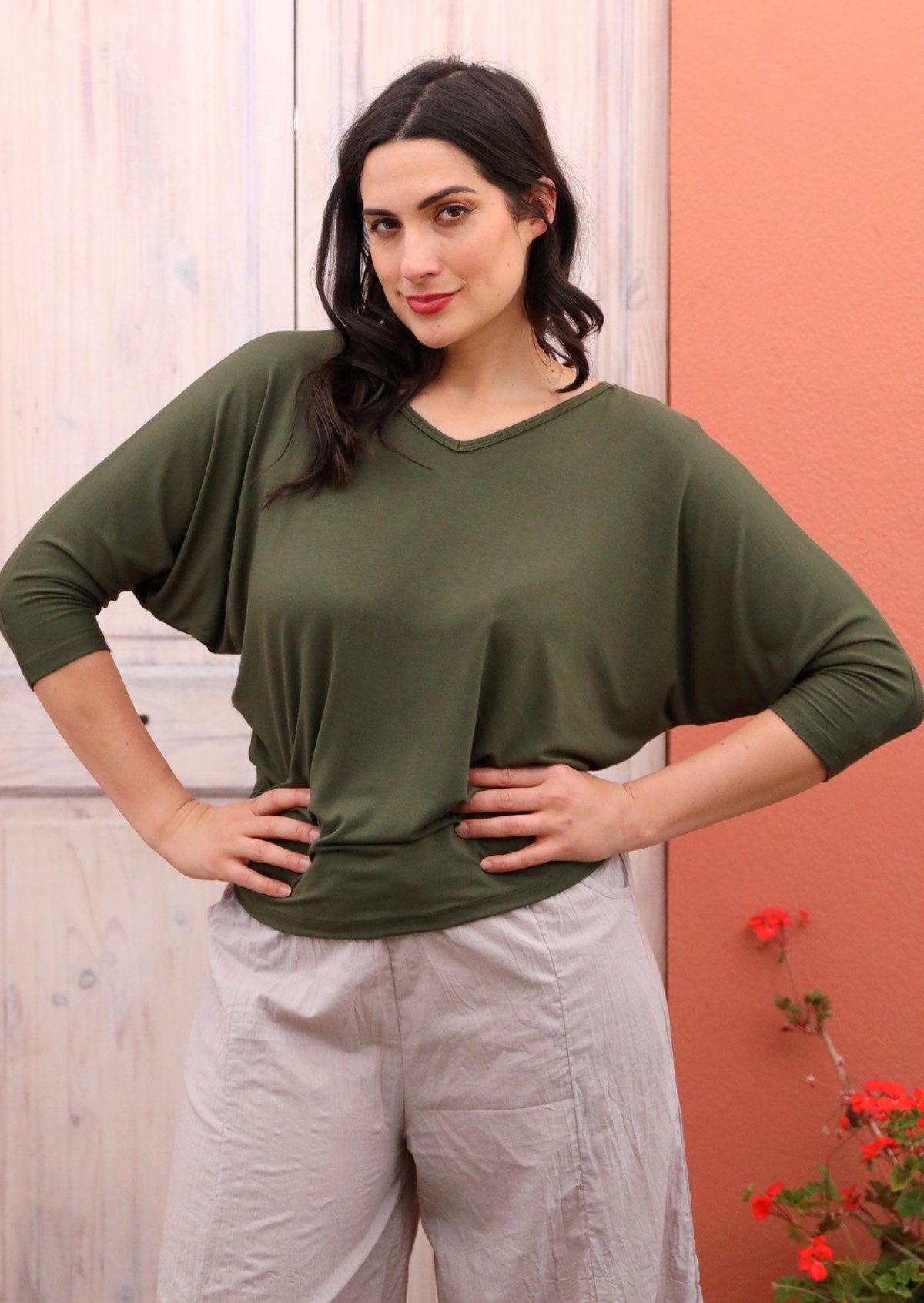 Woman wearing a 3/4 sleeve rayon batwing v-neck olive top with cream pants.