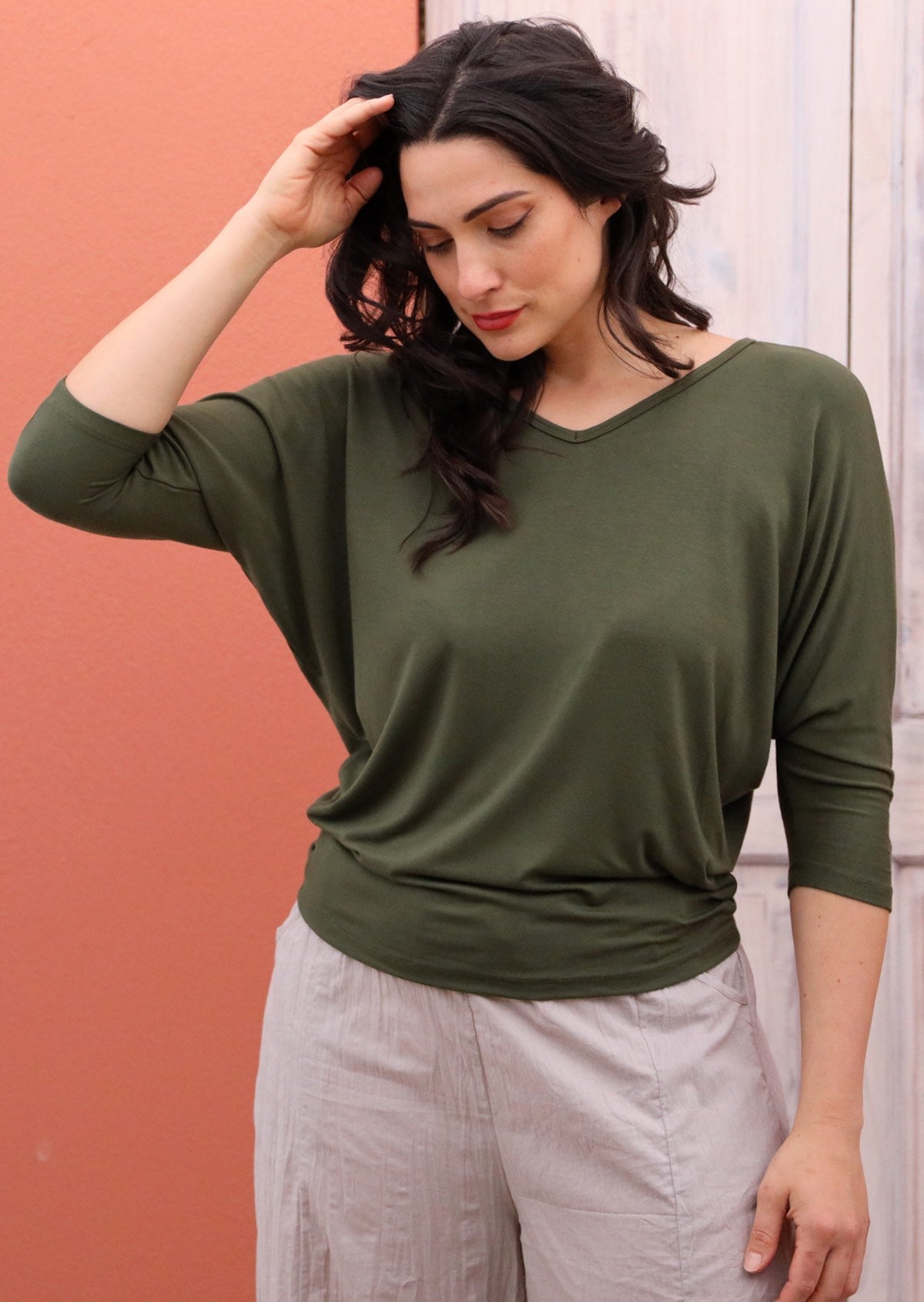 Woman with dark hair wearing a 3/4 sleeve rayon batwing v-neck olive top.