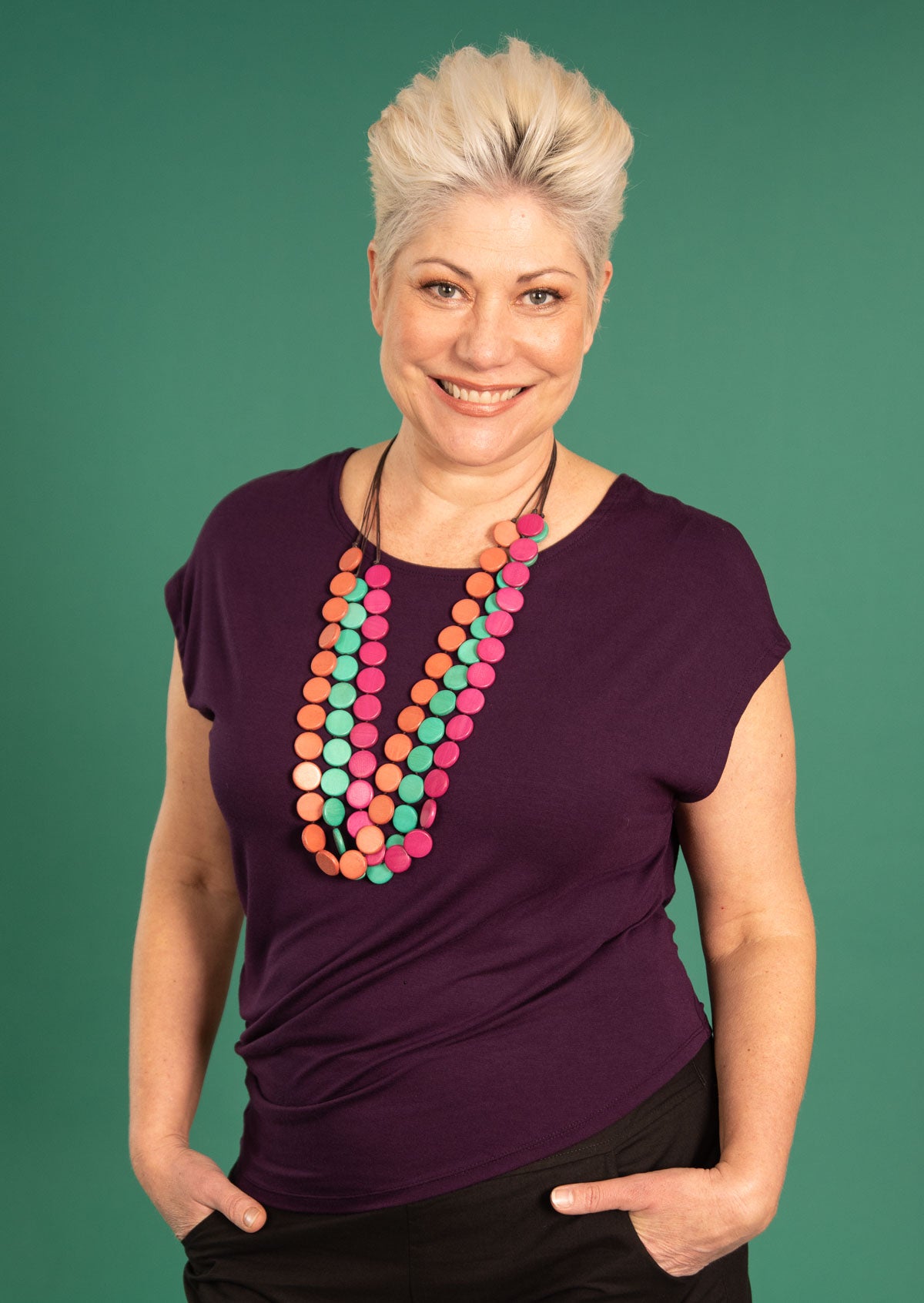 Woman wearing purple rayon t-shirt with side drape and bright coloured wooden beads