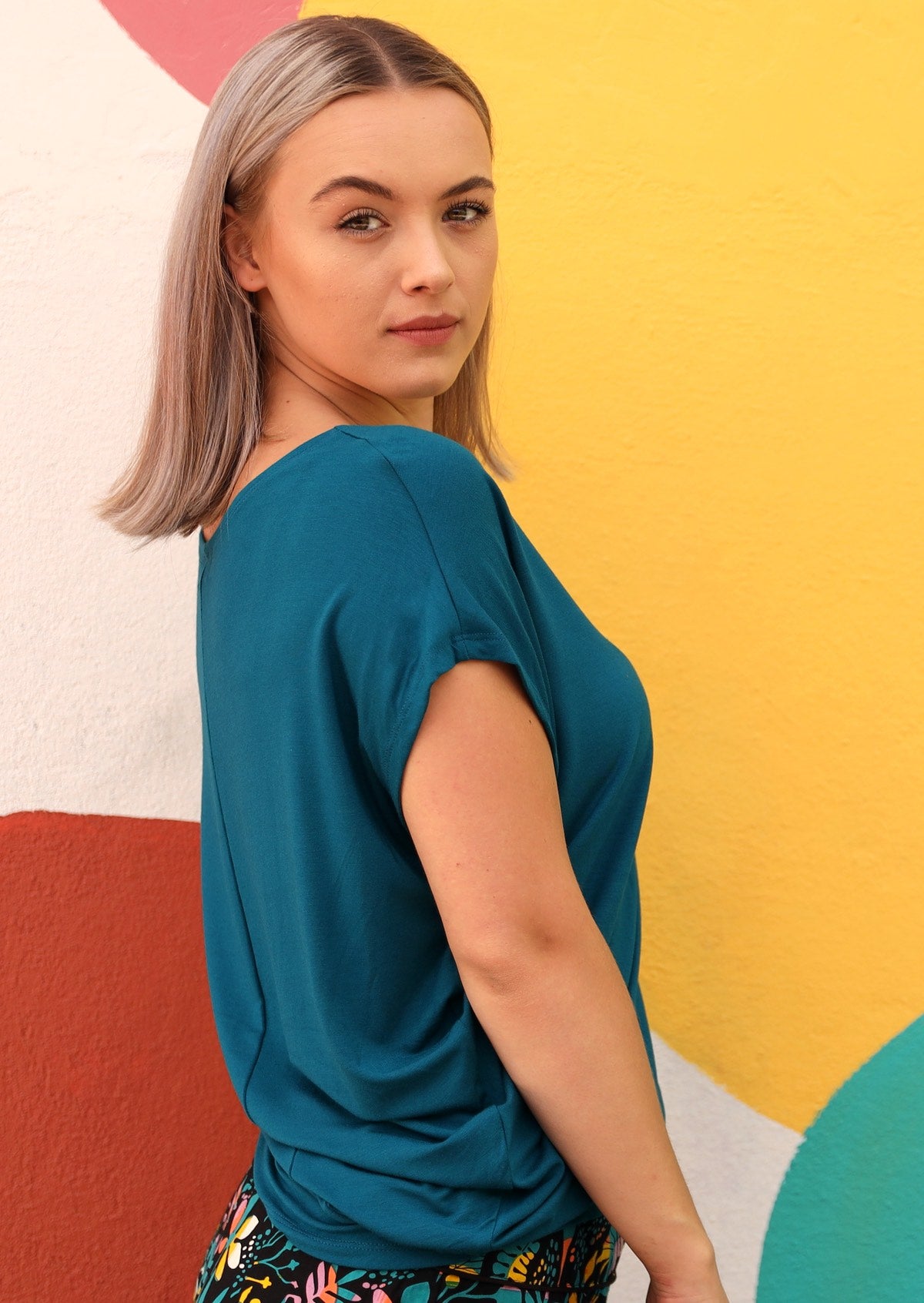 Woman wearing asymmetrical top in teal blue with colourful background