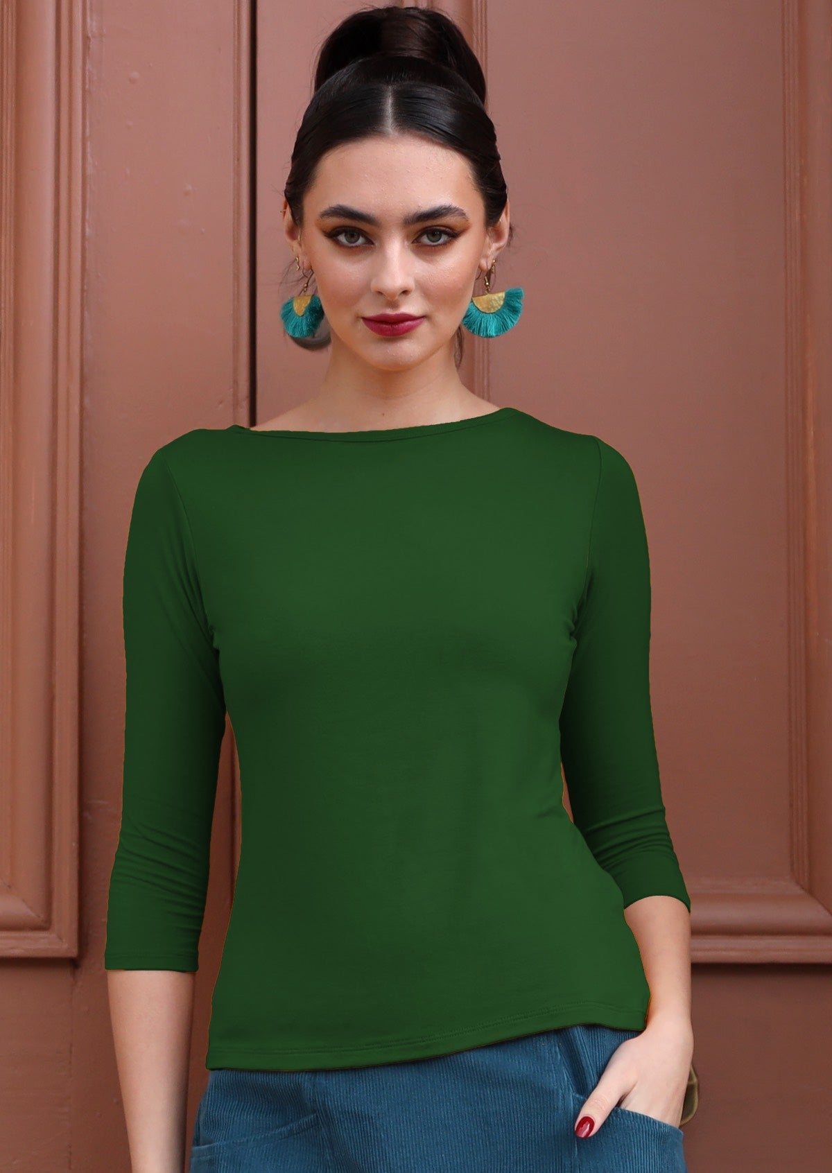 Woman wearing a rayon boat neck green 3/4 sleeve top and blue earrings.