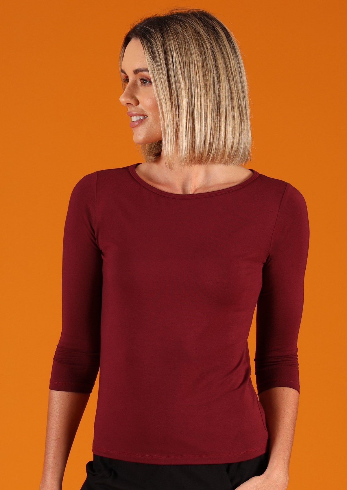 Woman wearing a rayon boat neck maroon 3/4 sleeve top looking to the side.