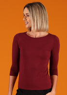 Woman wearing a rayon boat neck maroon 3/4 sleeve top looking to the side.