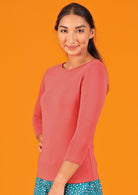 Woman wearing a rayon boat neck pink 3/4 sleeve top.