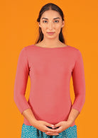 Woman wearing a rayon boat neck pink 3/4 sleeve top in front of orange background.
