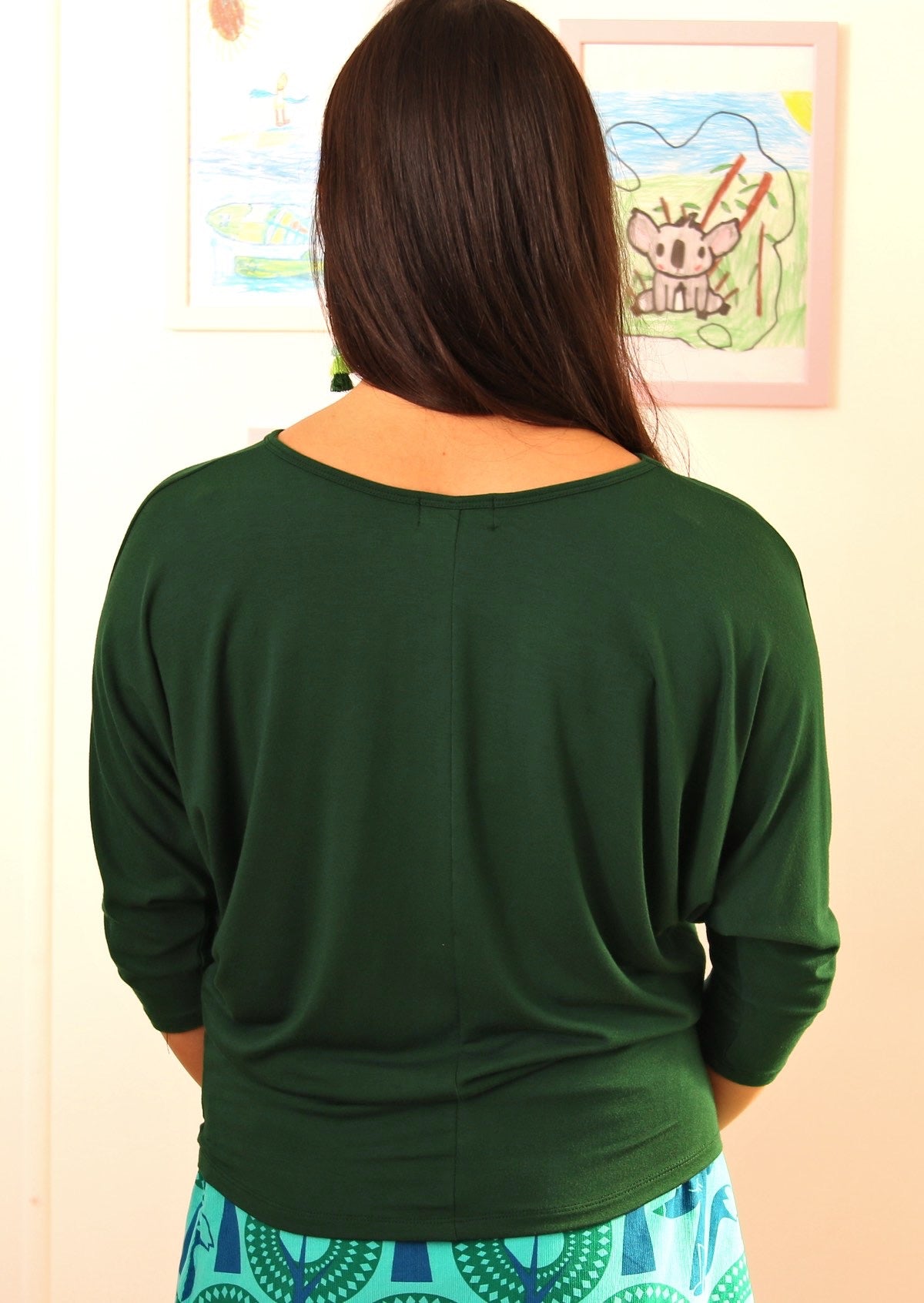 Back view of woman wearing a 3/4 sleeve rayon batwing round neckline green top.