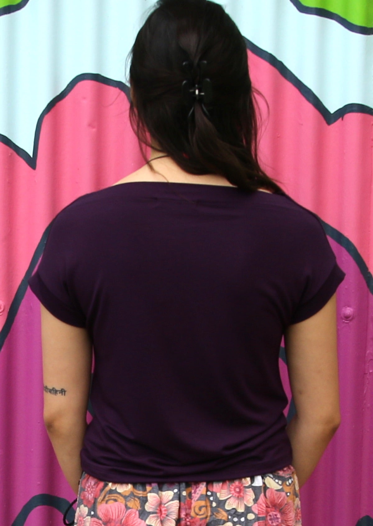 Back view of a woman wearing a wide neck mod purple stretch rayon boat neck top