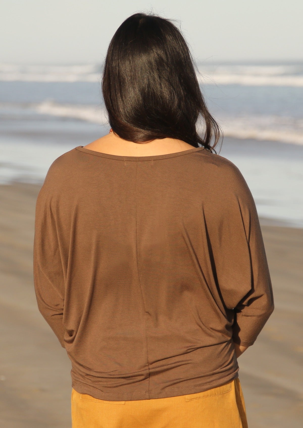 Back view of woman wearing a 3/4 sleeve rayon batwing round neckline brown top.