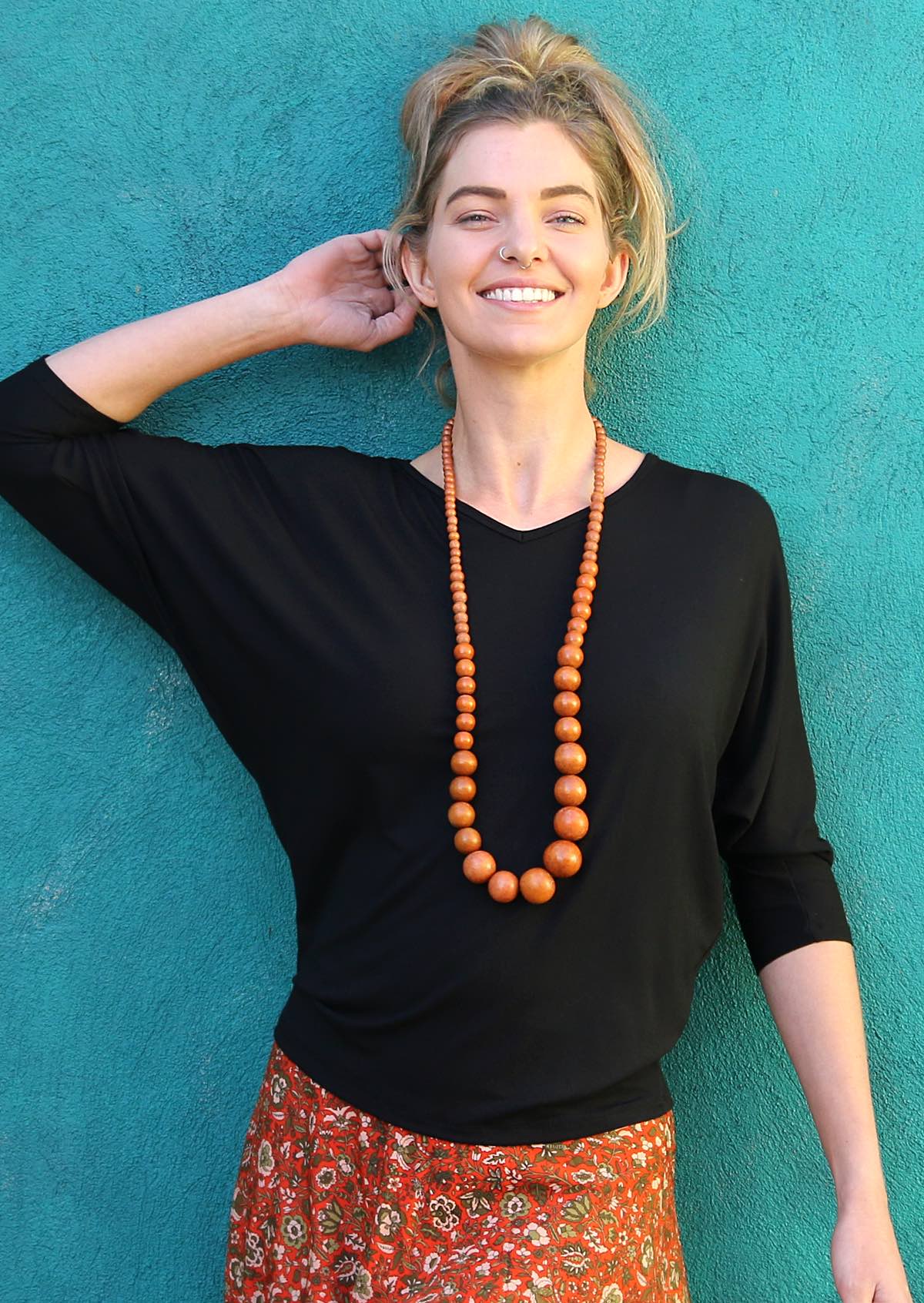 Woman wearing a 3/4 sleeve rayon batwing v-neck black top and wooden beads.
