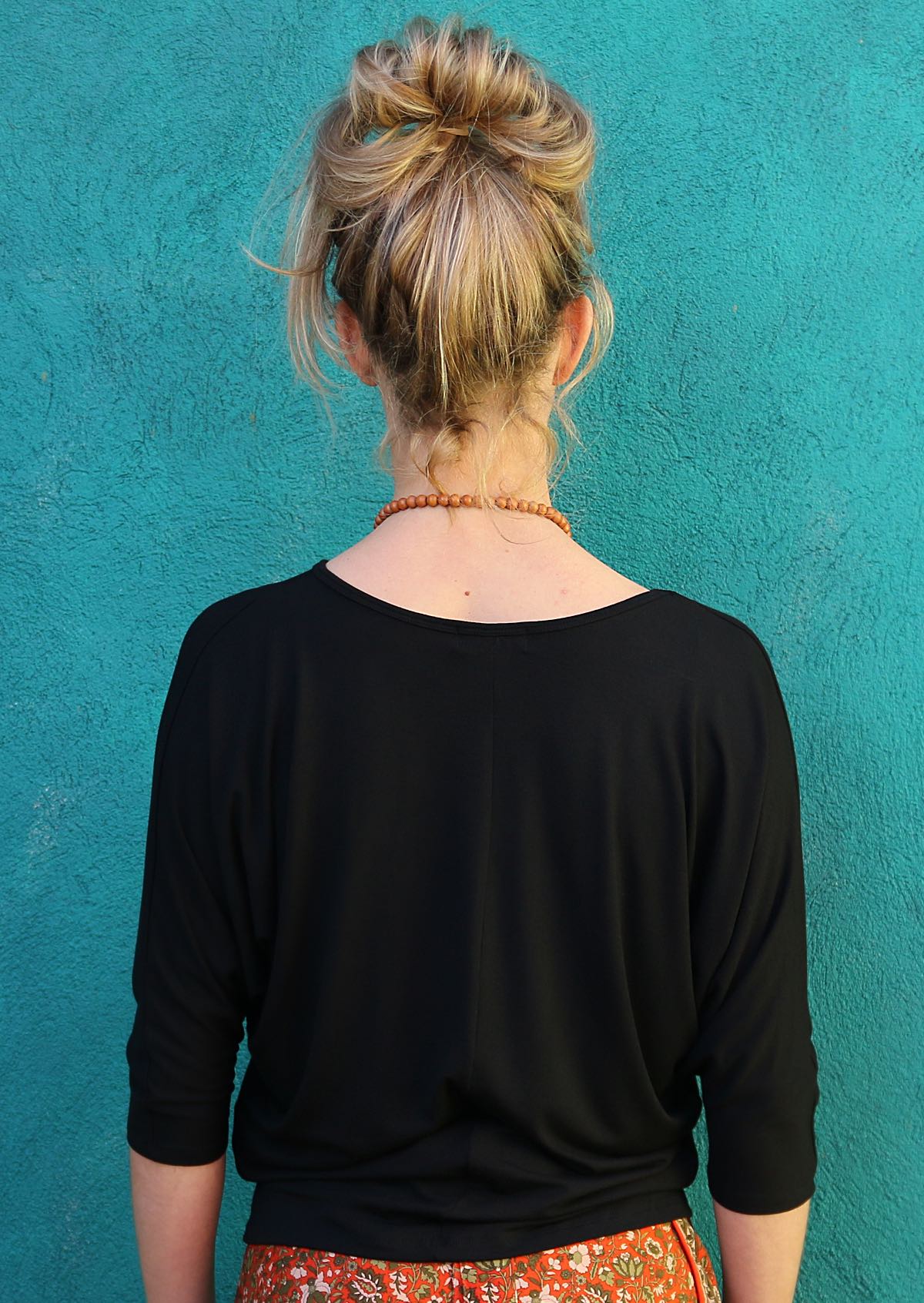 Back view of woman wearing a 3/4 sleeve rayon batwing v-neck black top.