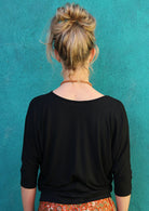 Back view of woman wearing a 3/4 sleeve rayon batwing v-neck black top.