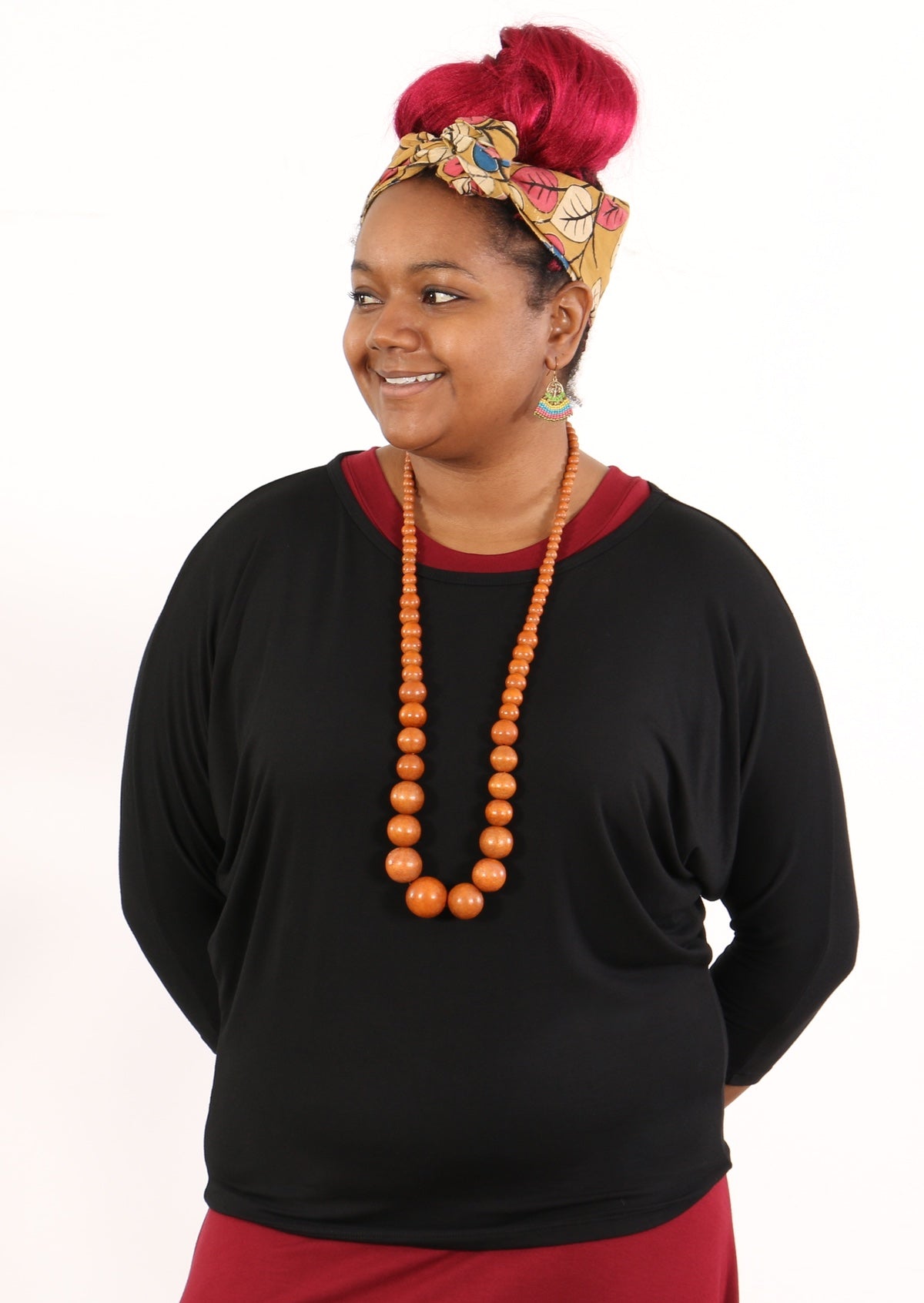 Woman wearing a 3/4 sleeve rayon batwing round neckline black top with orange beads and head scarf.