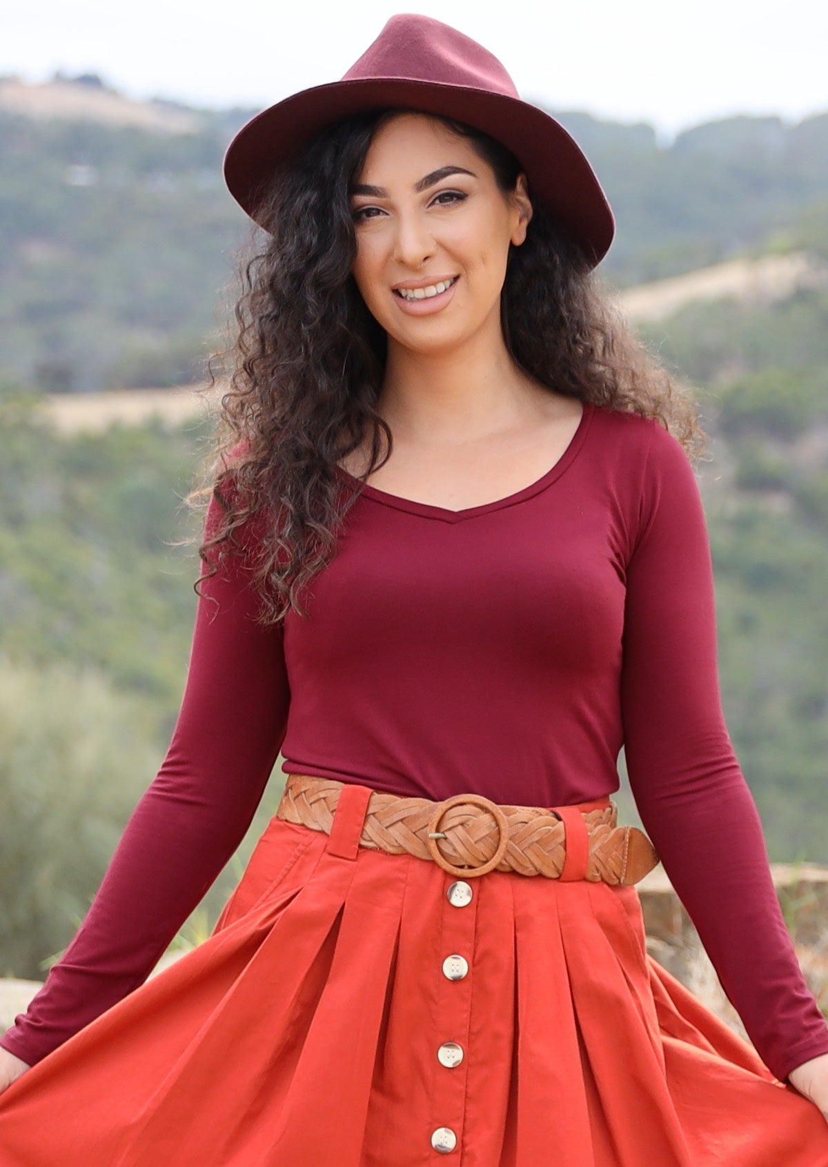 Woman wearing a maroon long sleeve stretch v-neck soft rayon top with red skirt and maroon hat.