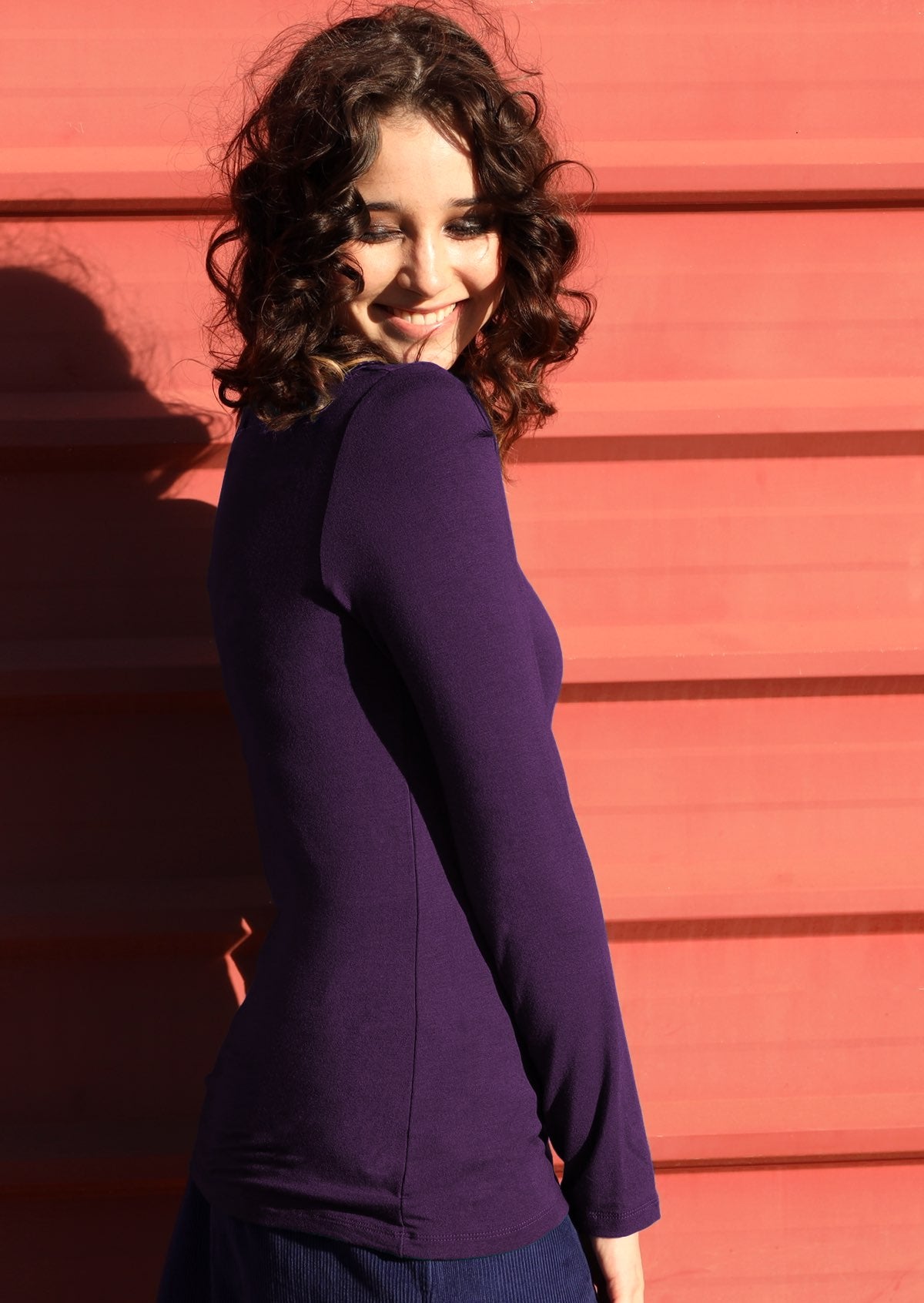 Side view of woman wearing purple long sleeve stretch v-neck soft rayon top.