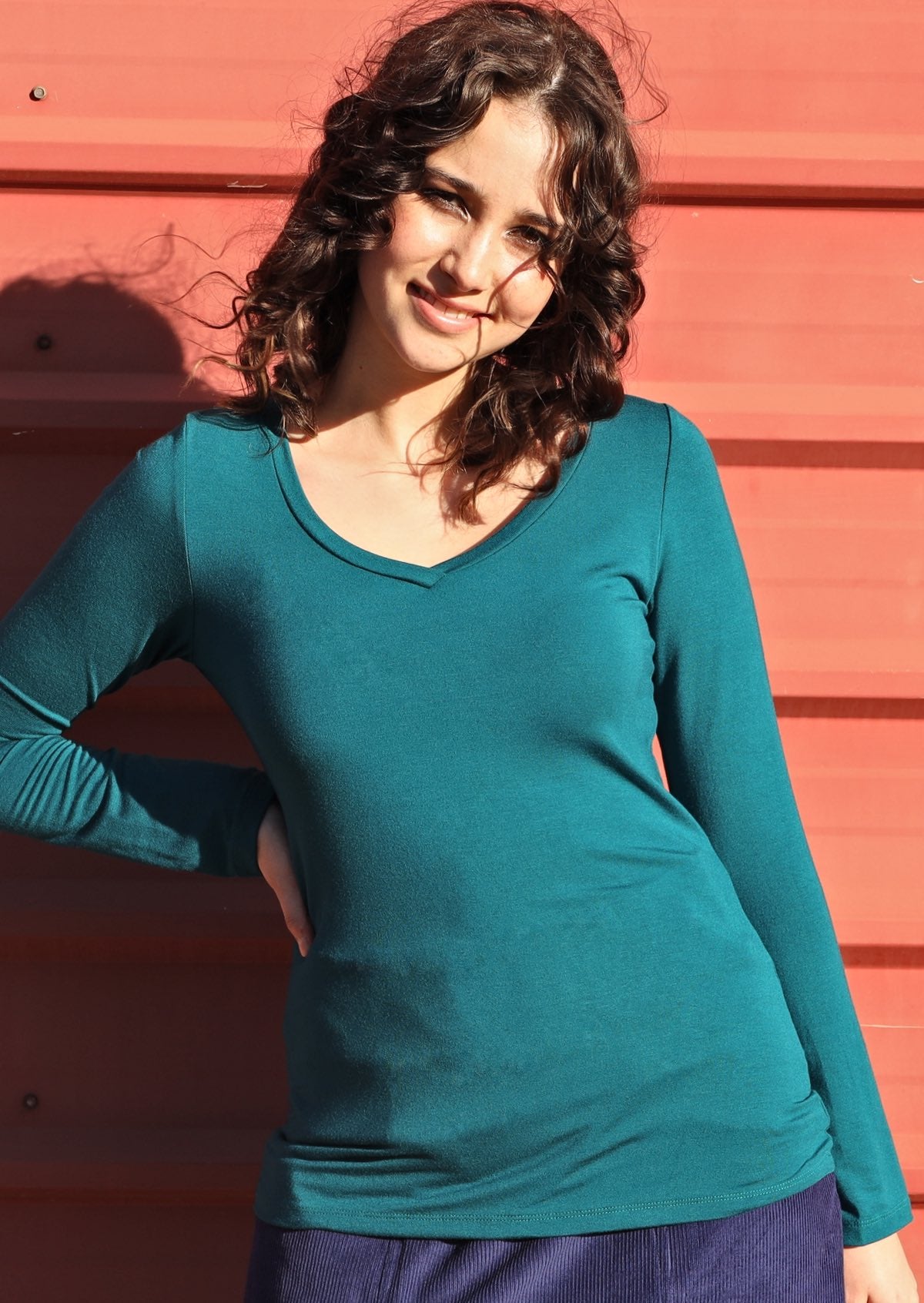 Woman with dark curly hair wearing a teal long sleeve stretch v-neck soft rayon top.