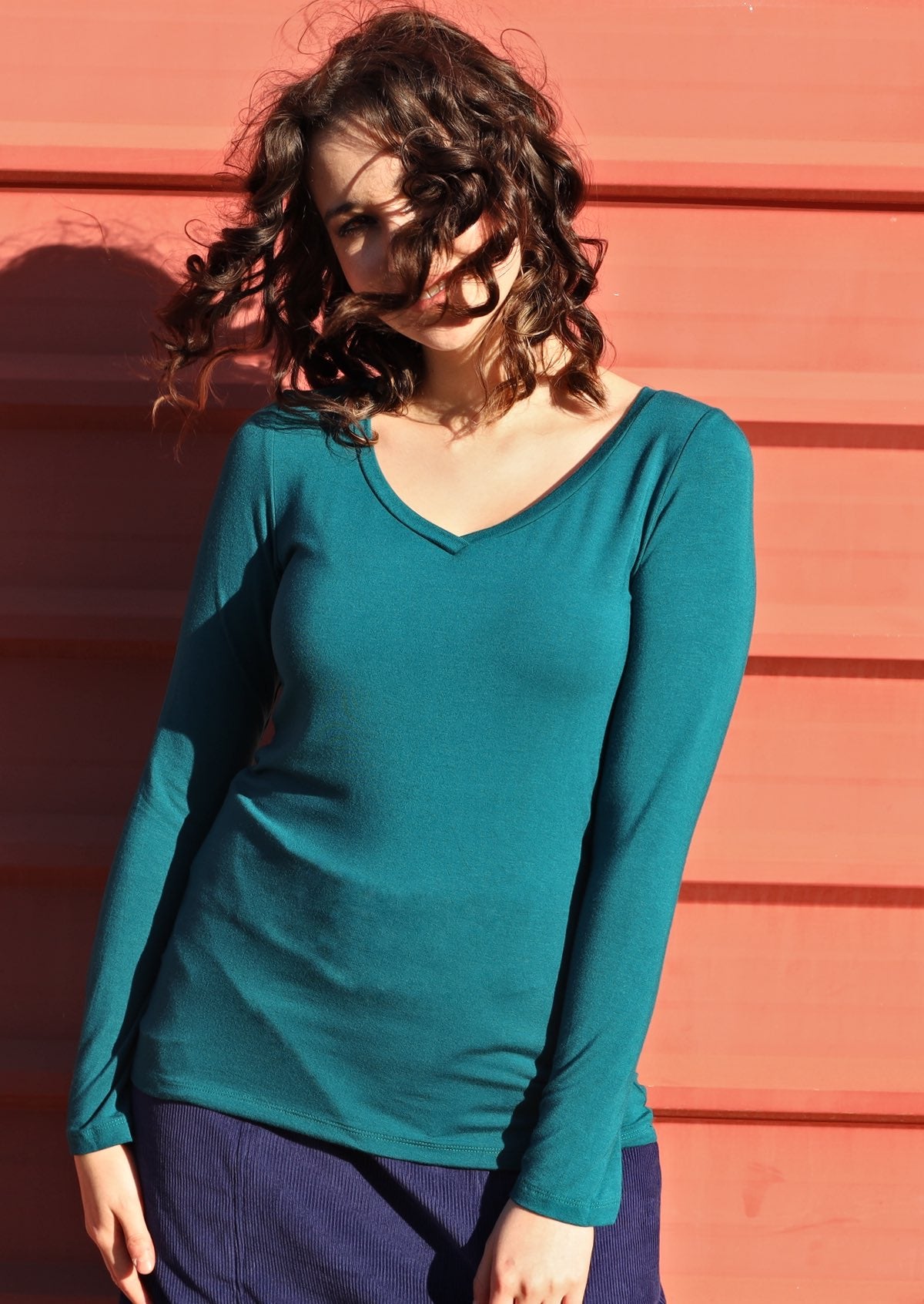 Woman wearing a teal long sleeve stretch v-neck soft rayon top in front of orange wall.