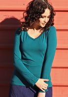 Woman wearing a teal long sleeve stretch v-neck soft rayon top with navy pants.