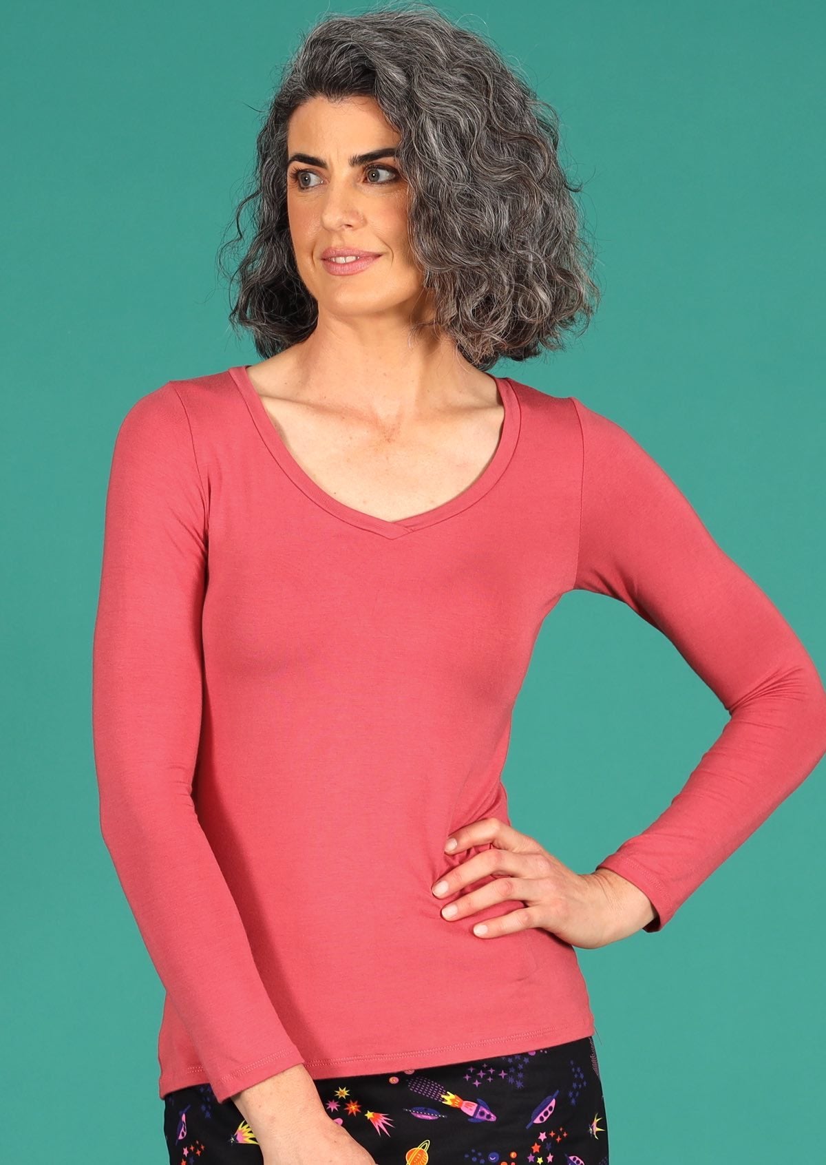Woman with grey wavy hair wearing a rose pink long sleeve stretch v-neck soft rayon top.